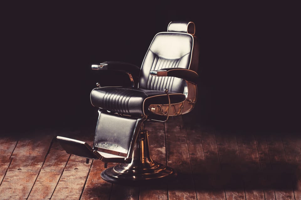 A vintage barber's chair, lit against a dark panelled wall on a worn wooden floor.